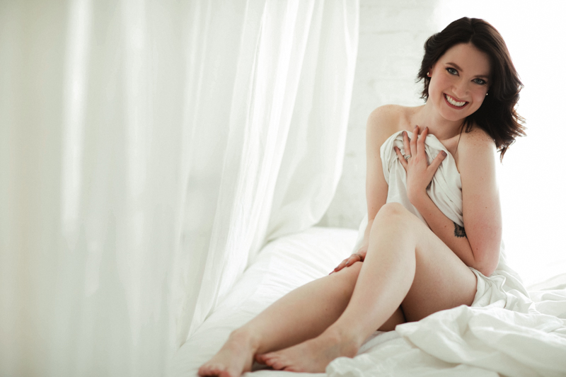 woman laughing wrapped in a sheet during her boudoir photoshoot